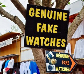 Humorous sign advertising "Genuine Fake Watches" at a market, symbolizing misleading but technically legal strategies—paralleling the fine line some taxpayers walk when attempting to avoid state income tax.