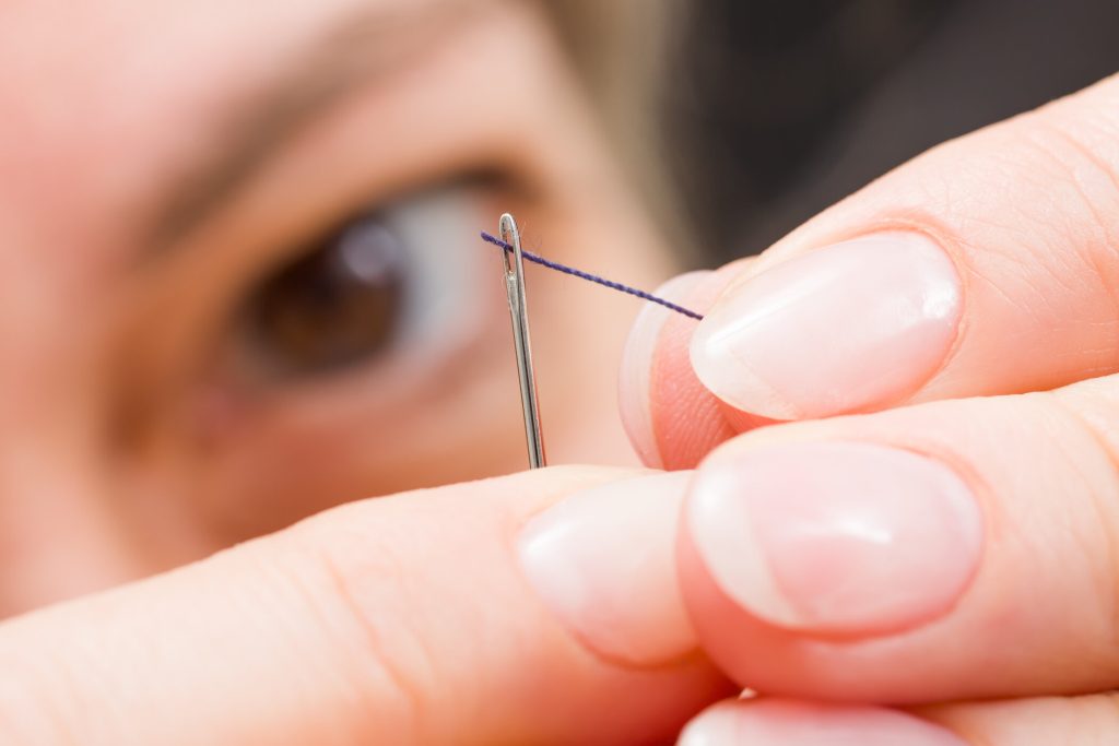 Woman fingers threading a needle. Showing how carefully a C-Corp and S-Corp hybrid must be done and the limited opening for it to work